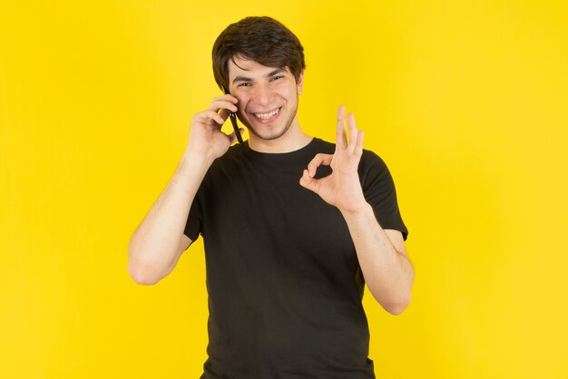 Retrato de un joven hablando por teléfono móvil contra amarillo.