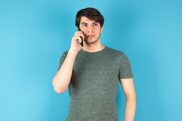 Retrato de un joven hablando por teléfono móvil contra azul.