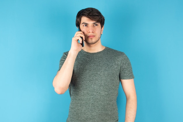 Retrato de un joven hablando por teléfono móvil contra azul.