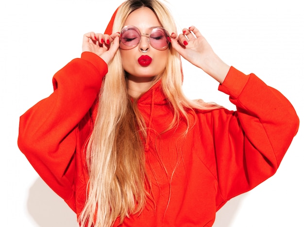 Retrato de joven hermosa chica mala inconformista en sudadera con capucha roja de moda y arete en la nariz. Modelo positivo divirtiéndose Aislado en blanco