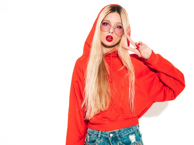 Retrato de joven hermosa chica mala inconformista en sudadera con capucha roja de moda y arete en la nariz. Modelo positivo divirtiéndose Aislado en blanco