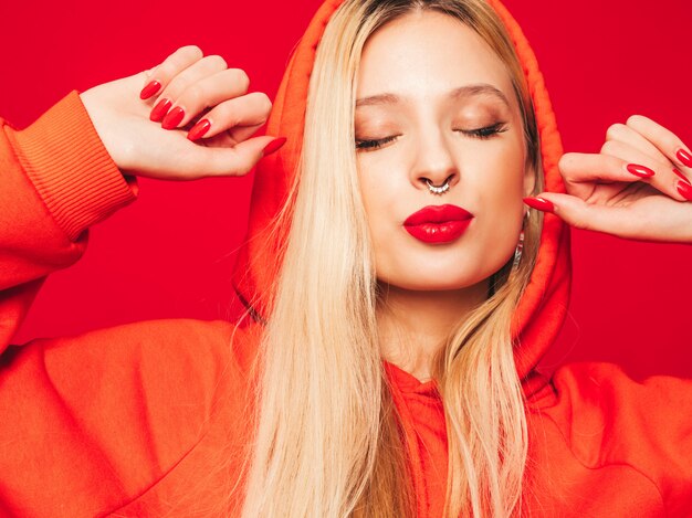 Retrato de joven hermosa chica mala inconformista en sudadera con capucha roja de moda y arete en la nariz. Modelo positivo