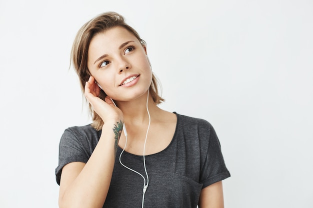 Retrato de joven hermosa chica soñadora escuchando música en auriculares sonriendo.