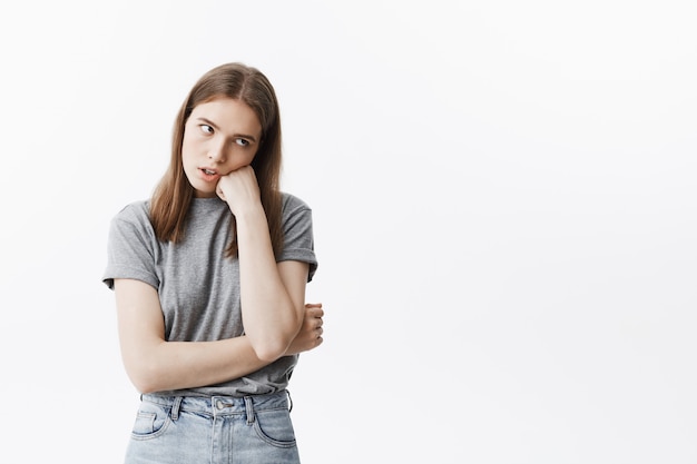 Retrato de joven hermosa estudiante infeliz chica con cabello oscuro en ropa casual mirando a un lado con expresión cansada, sosteniendo la cabeza con la mano, cabreado aburrido conferencia.