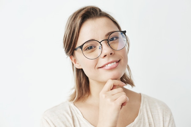 Retrato de joven hermosa en gafas sonriendo mano en el mentón.