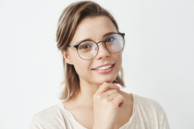 Retrato de joven hermosa en gafas sonriendo mano en el mentón.