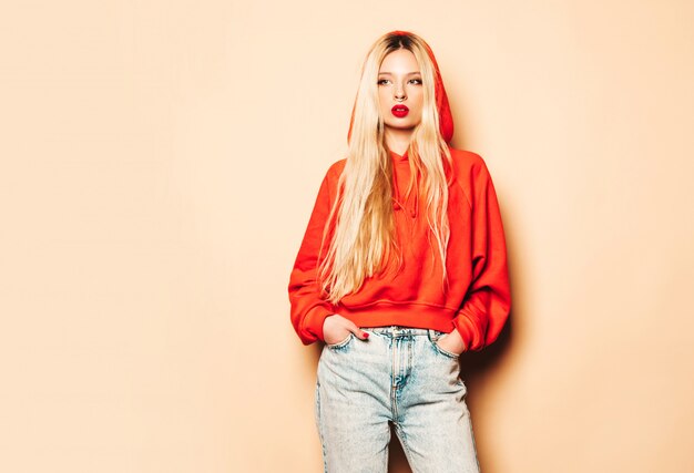 Retrato de joven hermosa hipster chica mala en sudadera con capucha roja de moda y arete en la nariz. Mujer rubia despreocupada sexy posando en estudio. Modelo positivo divirtiéndose