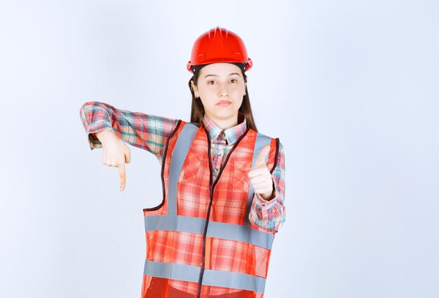 Retrato de joven hermosa ingeniera en casco apuntando a algún lugar.