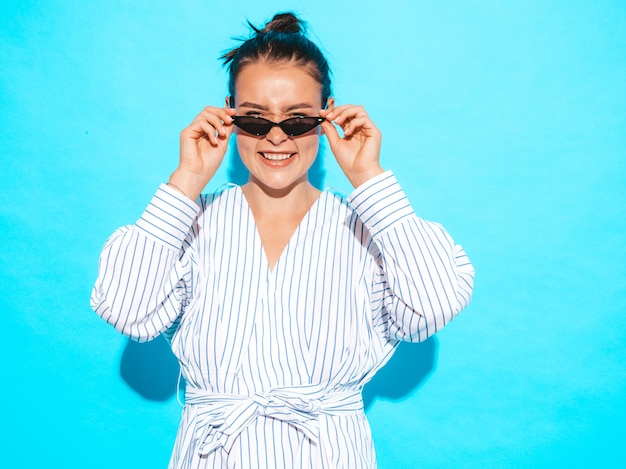 Foto gratuita retrato de joven hermosa muchacha sonriente hipster en ropa de moda de verano. mujer despreocupada sexy posando junto a la pared azul. modelo positivo divirtiéndose en gafas de sol