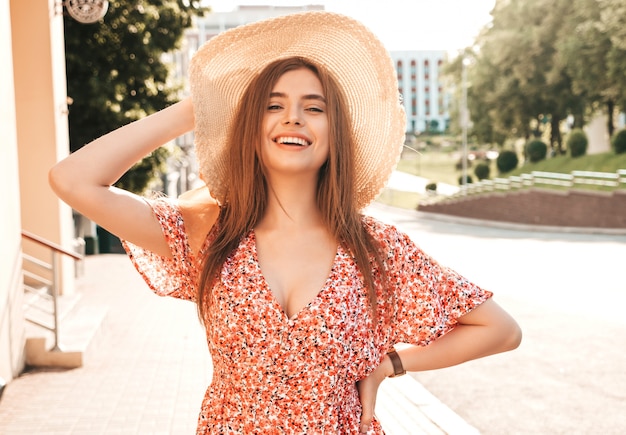 Retrato de joven hermosa muchacha sonriente hipster en verano vestido de verano. Mujer despreocupada sexy posando en el fondo de la calle con sombrero al atardecer. Modelo positivo al aire libre