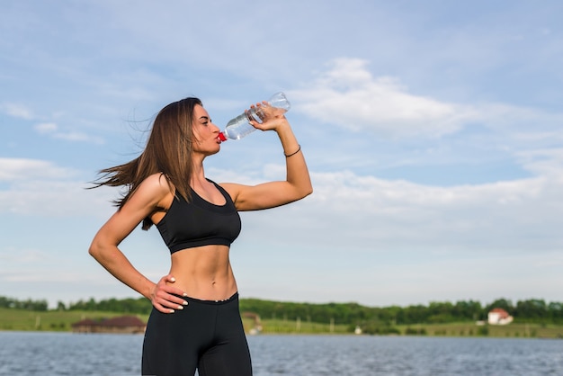 Retrato de joven hermosa mujer bebiendo agua en el parque de verano verde.