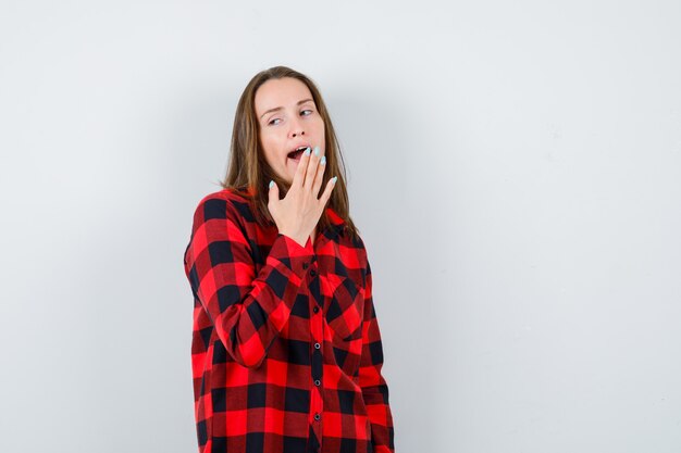 Retrato de joven hermosa mujer bostezando, mirando a otro lado en camisa casual y mirando soñolienta vista frontal