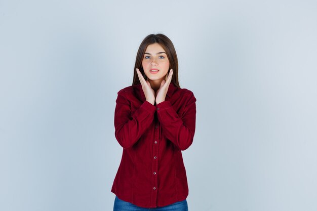 Retrato de joven hermosa mujer cogidos de la mano cerca de la cara en camisa y mirando alegre