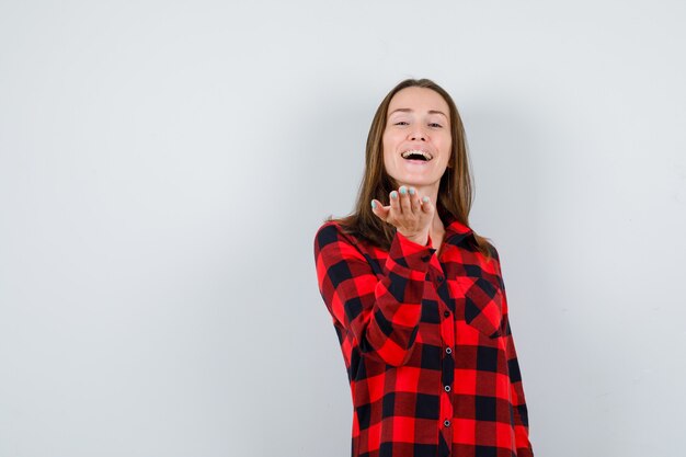 Retrato de joven hermosa mujer fingiendo sostener algo en camisa casual y mirando alegre vista frontal