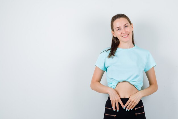 Retrato de joven hermosa mujer con las manos delante de ella en camiseta, pantalones y mirando alegre vista frontal