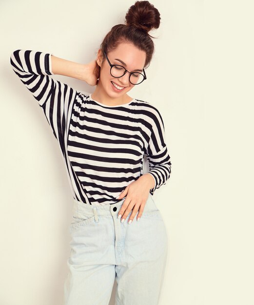 Retrato de joven hermosa mujer morena modelo chica con maquillaje desnudo en gafas en ropa hipster de verano posando junto a la pared.