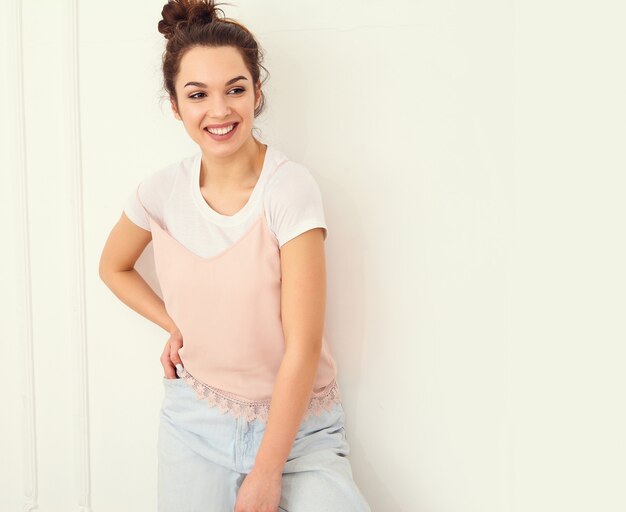 Retrato de joven hermosa mujer morena modelo chica con maquillaje desnudo en ropa de verano colorido hipster rosa posando junto a la pared. mirando felizmente