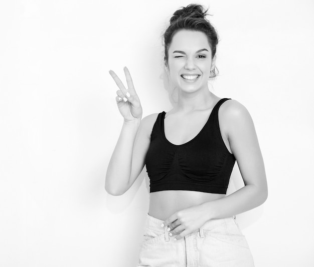 Foto gratuita retrato de joven hermosa mujer morena modelo chica con maquillaje desnudo en verano camiseta top y jeans ropa posando junto a la pared. guiñando un ojo y mostrando el signo de la paz