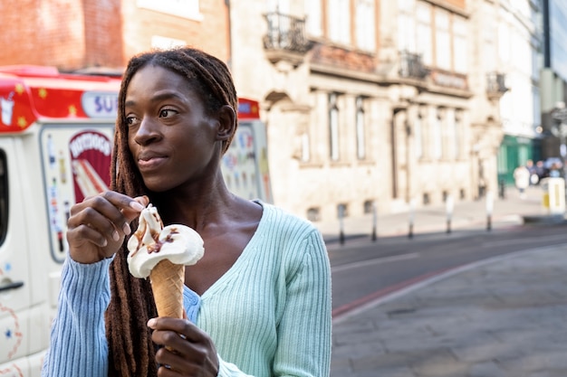 Retrato de una joven hermosa mujer con rastas afro disfrutando de un helado en la ciudad