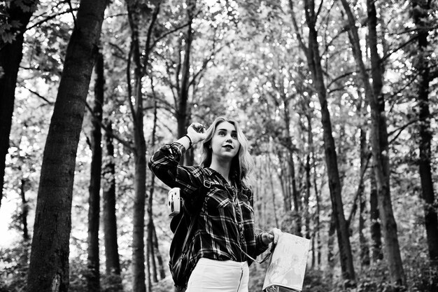 Retrato de una joven y hermosa mujer rubia con camisa de tartán sosteniendo un mapa en el bosque