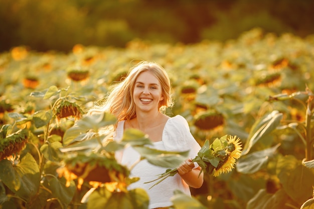 Retrato de joven hermosa mujer rubia en campo de girasoles en luz trasera. Concepto de campo de verano Mujer y girasoles. Luz de verano. Belleza al aire libre.