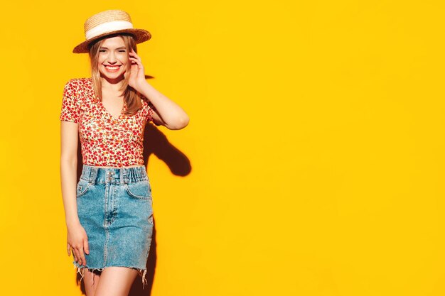 Retrato de joven hermosa mujer rubia sonriente en ropa de verano de moda mujer despreocupada posando cerca de la pared amarilla en el estudio Modelo positivo divirtiéndose en el interior Alegre y feliz Con sombrero