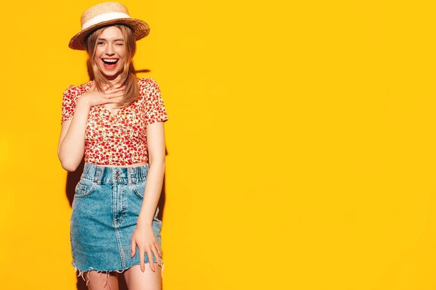 Retrato de joven hermosa mujer rubia sonriente en ropa de verano de moda mujer despreocupada posando cerca de la pared amarilla en el estudio Modelo positivo divirtiéndose en el interior Alegre y feliz Con sombrero