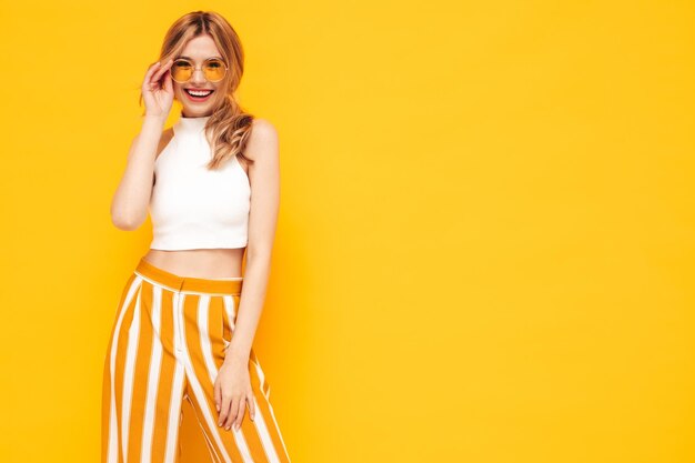 Retrato de joven hermosa mujer rubia sonriente en ropa de verano de moda mujer despreocupada posando cerca de la pared amarilla en el estudio Modelo positivo divirtiéndose en el interior Alegre y feliz