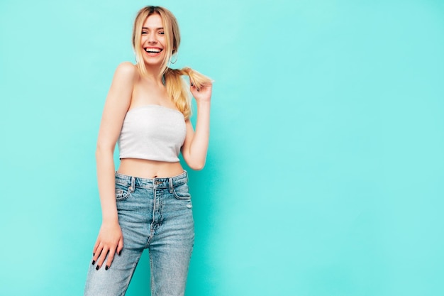 Retrato de joven hermosa mujer rubia sonriente en ropa de verano de moda Mujer sexy despreocupada posando junto a la pared azul en el estudio Modelo positivo divirtiéndose en el interior Alegre y feliz