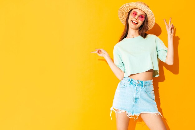 Foto gratuita retrato de joven hermosa mujer sonriente en jeans de moda de verano falda mujer despreocupada posando cerca de la pared amarilla en el estudio modelo positivo divirtiéndose en el interior alegre y feliz con sombrero