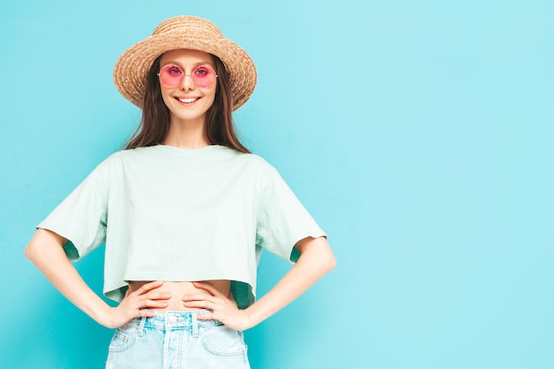 Retrato de joven hermosa mujer sonriente en jeans de verano de moda falda mujer despreocupada posando cerca de la pared azul en el estudio Modelo positivo divirtiéndose en el interior Alegre y feliz Con sombrero