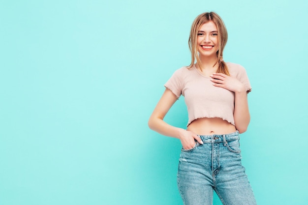 Retrato de joven hermosa mujer sonriente en ropa de verano de moda Mujer sexy despreocupada posando cerca de la pared azul en el estudio Modelo rubio positivo divirtiéndose y volviéndose loco Alegre y feliz