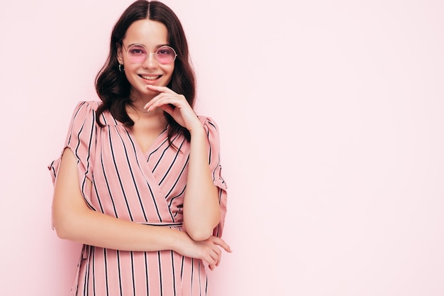 Retrato de joven hermosa mujer sonriente en vestido rosa de verano de moda Mujer sexy despreocupada posando junto a la pared en el estudio Modelo positivo divirtiéndose en el interior Alegre y feliz En gafas de sol