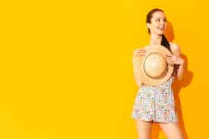 Foto gratuita retrato de joven hermosa mujer sonriente en vestido de verano de moda mujer despreocupada posando cerca de la pared amarilla en el estudio modelo positivo divirtiéndose en el interior alegre y feliz sosteniendo el sombrero en las manos