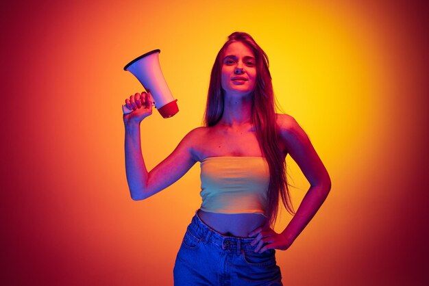 Retrato de una joven hermosa mujer sosteniendo un megáfono aislado sobre un fondo rojo amarillo con luz de neón