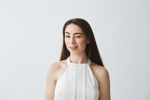 Retrato de joven hermosa niña tierna en blusa guiño sonriendo.