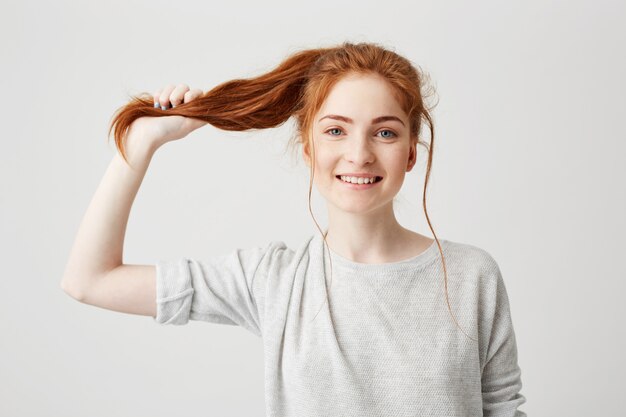 Retrato de joven hermosa pelirroja tocando su cola de pelo.