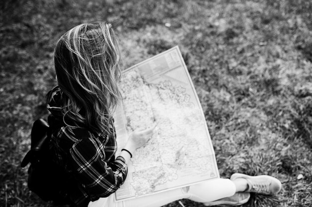 Retrato de una joven y hermosa rubia positiva sentada en el suelo con un mapa en sus manos en el bosque