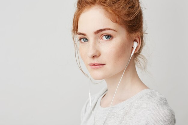 Retrato de joven hermosa tierna pelirroja con ojos azules en auriculares sonriendo.