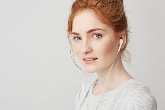 Retrato de joven hermosa tierna pelirroja con ojos azules en auriculares sonriendo.