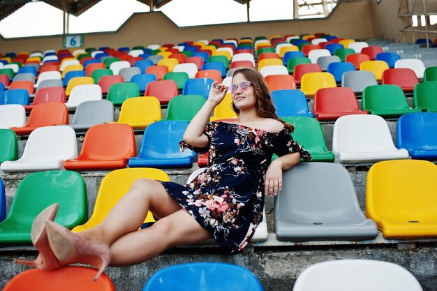 Retrato de una joven hermosa vestida y gafas de sol sentada en las tribunas del estadio