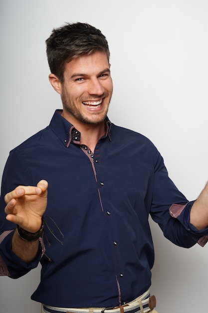 Retrato de un joven hispano alegre con una camisa azul posando contra una pared blanca