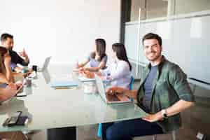 Foto gratuita retrato de un joven hispano sentado con colegas en la sala de reuniones