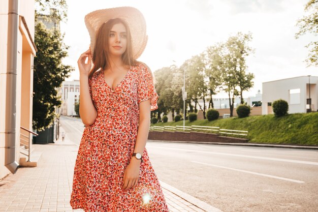 Retrato de joven inconformista hermosa chica en vestido de verano de moda. Mujer despreocupada sexy posando en el fondo de la calle con sombrero al atardecer. Modelo positivo al aire libre