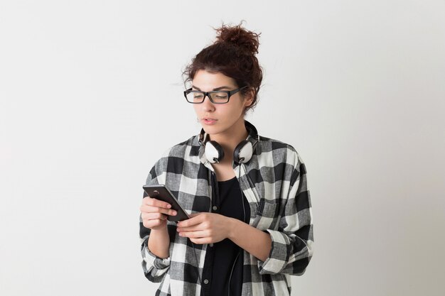 Retrato de joven inconformista sonriente mujer bonita en camisa a cuadros con gafas posando aislado, sosteniendo teléfono inteligente