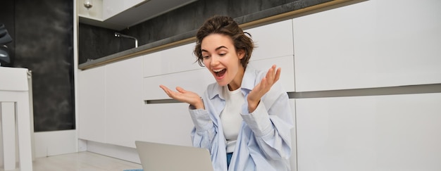 Foto gratuita retrato de una joven independiente que se conecta a reuniones en línea, chats de video en una computadora portátil, se sienta en la cocina.