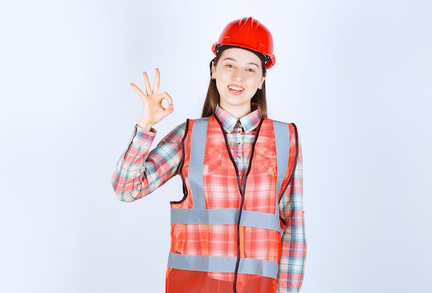 Retrato de joven ingeniera en casco dando señal ok.