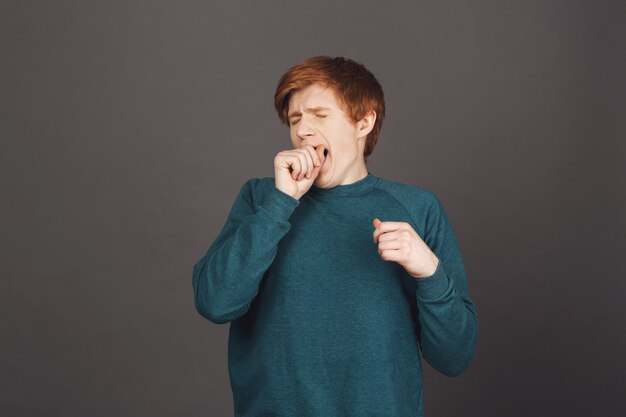 Retrato de joven jengibre europeo con corte de pelo corto en ropa casual suéter verde boca con mano