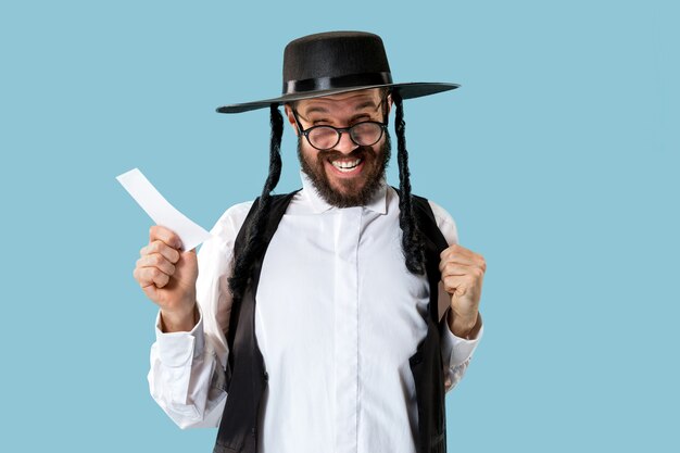 Retrato de un joven judío ortodoxo con boleta de apuestas en el estudio. Vacaciones, celebración, judaísmo, concepto de apuestas.