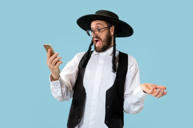 Retrato de un joven judío ortodoxo con teléfono móvil en el estudio. Purim, negocios, empresario, festival, fiesta, celebración, judaísmo, concepto de religión.